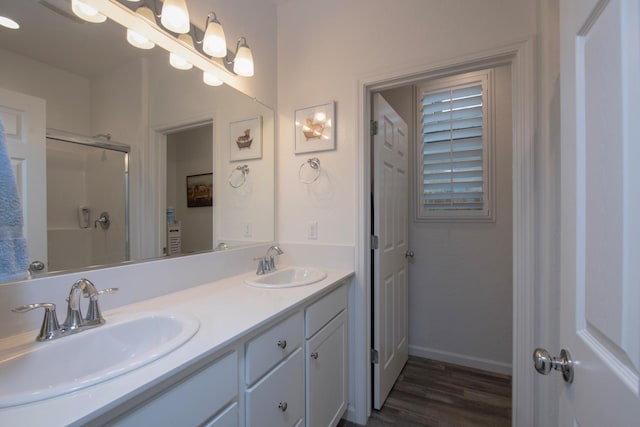 bathroom with double vanity, an enclosed shower, a sink, and baseboards