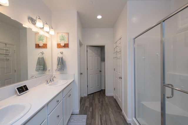 full bath featuring double vanity, a stall shower, a sink, and wood finished floors