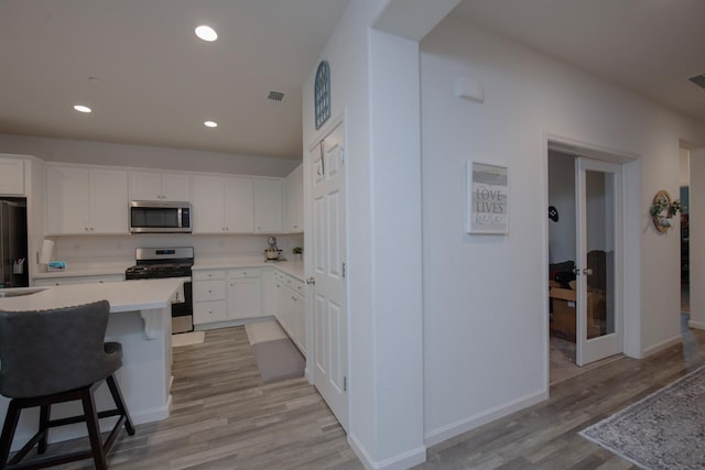 kitchen featuring stainless steel appliances, light countertops, light wood-type flooring, white cabinetry, and recessed lighting