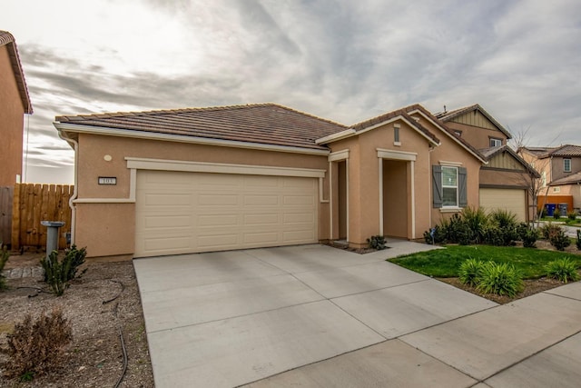 view of front of property with a tile roof, stucco siding, fence, a garage, and driveway