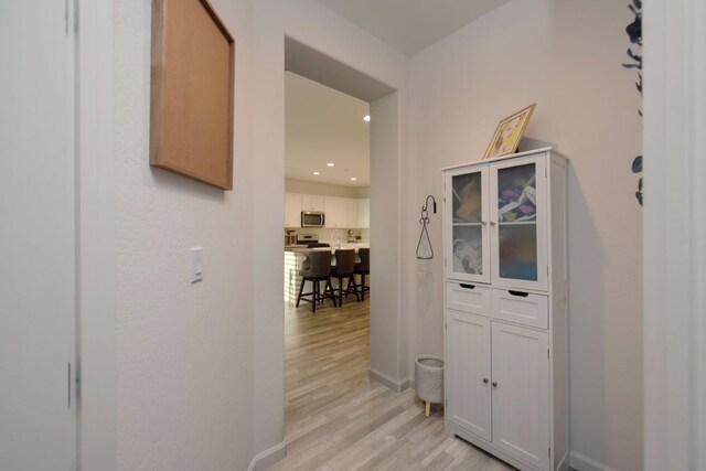 hallway featuring light wood finished floors, baseboards, and recessed lighting