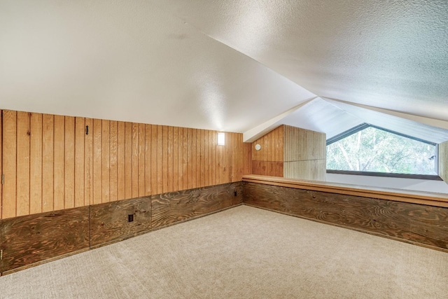 additional living space featuring carpet floors, wooden walls, a textured ceiling, and lofted ceiling