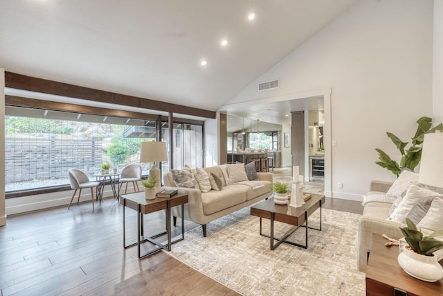 living area with high vaulted ceiling, recessed lighting, wood finished floors, visible vents, and baseboards