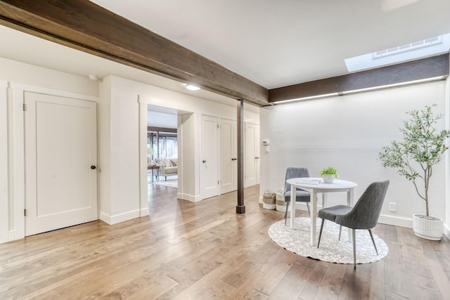 sitting room featuring a skylight, visible vents, baseboards, light wood-type flooring, and beam ceiling