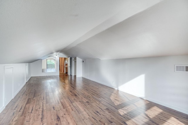 additional living space featuring vaulted ceiling, wood finished floors, visible vents, and baseboards