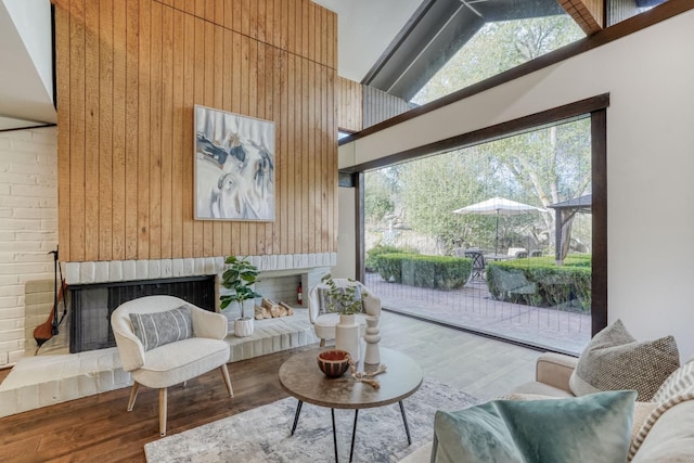 sitting room featuring high vaulted ceiling, wood walls, a brick fireplace, and wood finished floors