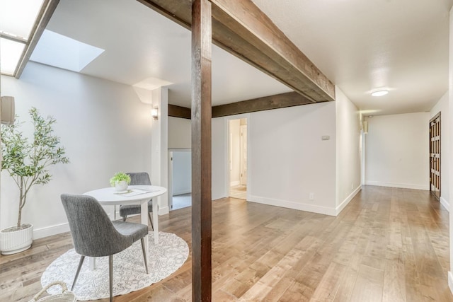 dining space with a skylight, baseboards, beamed ceiling, and light wood finished floors