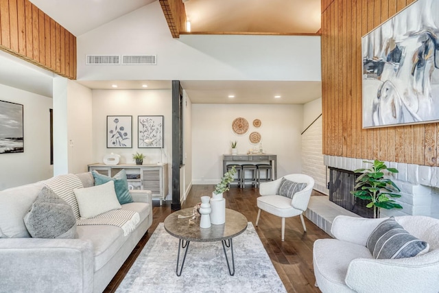 living area with high vaulted ceiling, a brick fireplace, visible vents, and dark wood-type flooring