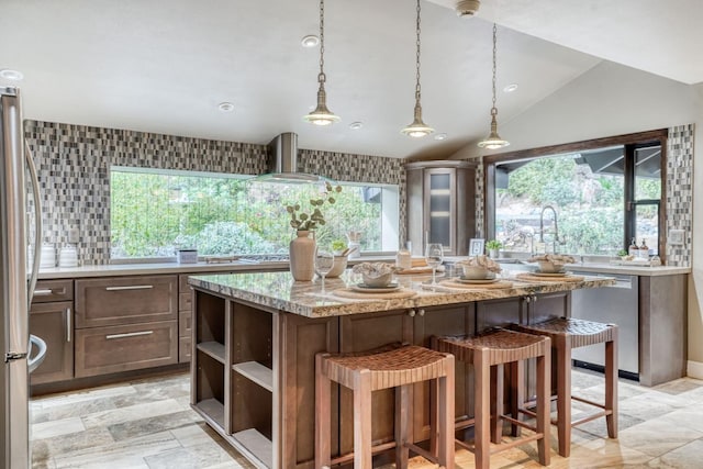 kitchen with appliances with stainless steel finishes, a sink, vaulted ceiling, light stone countertops, and wall chimney exhaust hood