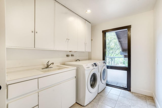 laundry area featuring cabinet space, light tile patterned floors, baseboards, washer and clothes dryer, and a sink