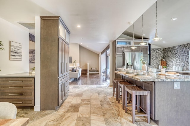 kitchen featuring light stone counters, a breakfast bar area, a spacious island, hanging light fixtures, and stainless steel fridge