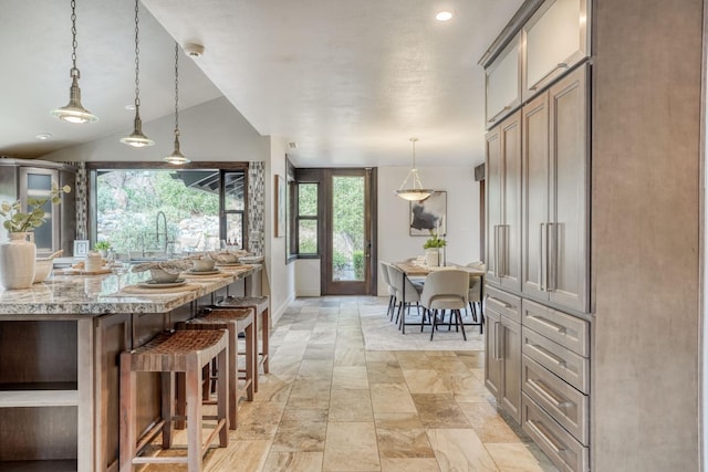 kitchen with decorative light fixtures, lofted ceiling, a sink, light stone countertops, and a kitchen breakfast bar