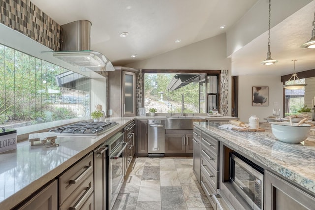 kitchen with stainless steel appliances, exhaust hood, vaulted ceiling, light stone countertops, and decorative light fixtures