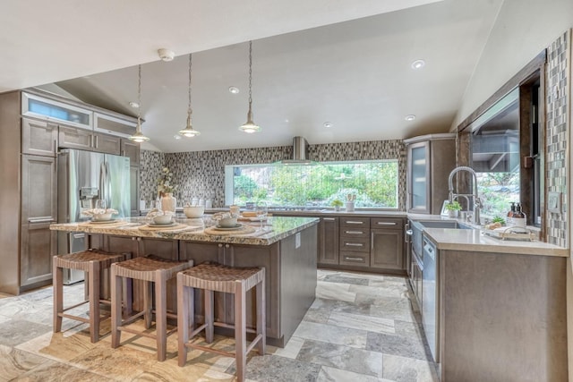 kitchen featuring appliances with stainless steel finishes, wall chimney range hood, a center island, a kitchen bar, and stone tile flooring