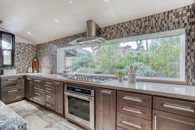 kitchen with lofted ceiling, light stone counters, appliances with stainless steel finishes, wall chimney exhaust hood, and tasteful backsplash