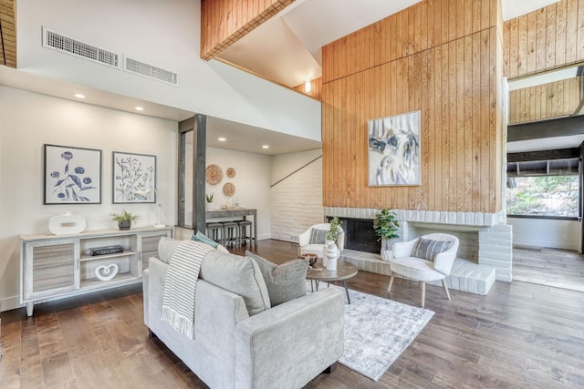 living area with a towering ceiling, visible vents, a fireplace with raised hearth, and dark wood-type flooring