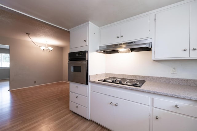 kitchen featuring light countertops, wall oven, light wood-style floors, under cabinet range hood, and black electric cooktop