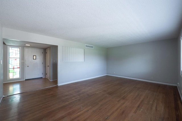 empty room featuring baseboards, visible vents, dark wood finished floors, and a textured ceiling