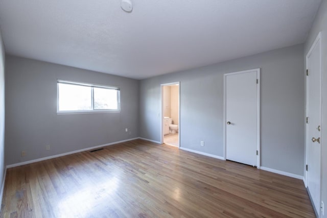 unfurnished bedroom featuring ensuite bath, visible vents, baseboards, and wood finished floors