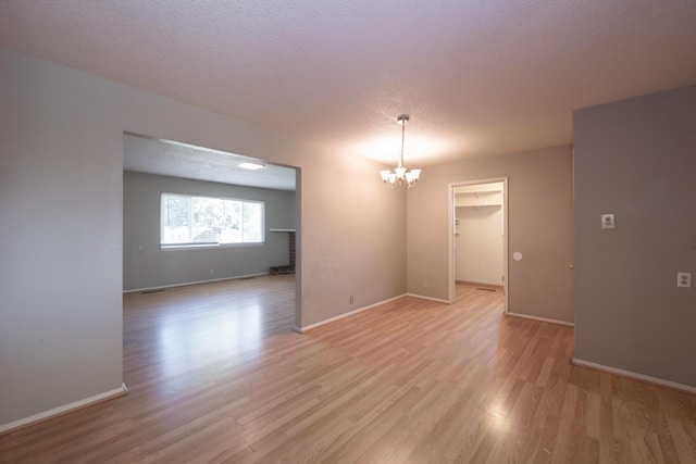 empty room featuring a chandelier, a textured ceiling, light wood-type flooring, and baseboards