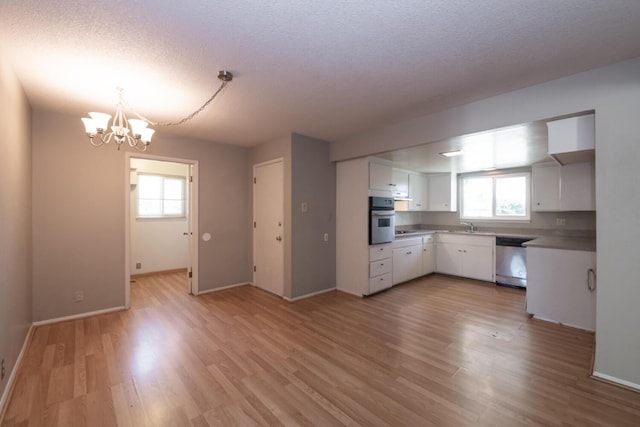 kitchen featuring an inviting chandelier, appliances with stainless steel finishes, light wood-style floors, white cabinetry, and a textured ceiling