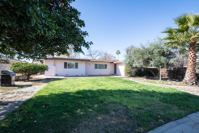 rear view of house featuring fence, a lawn, and stucco siding