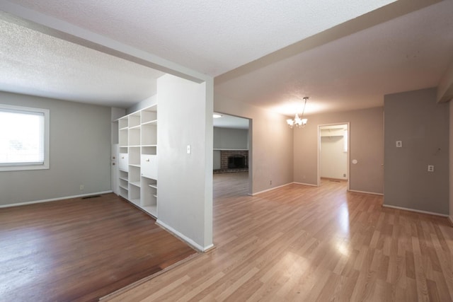 empty room featuring a textured ceiling, a notable chandelier, visible vents, light wood-type flooring, and a brick fireplace