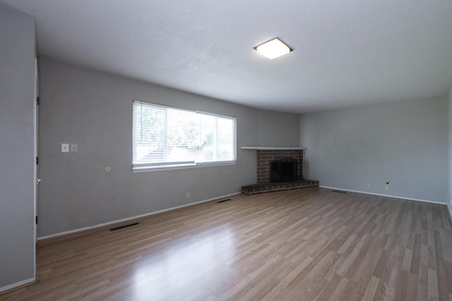 unfurnished living room featuring a textured ceiling, light wood-style flooring, a fireplace, and visible vents