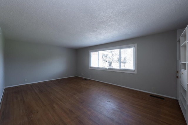 unfurnished room with dark wood-type flooring, visible vents, a textured ceiling, and baseboards