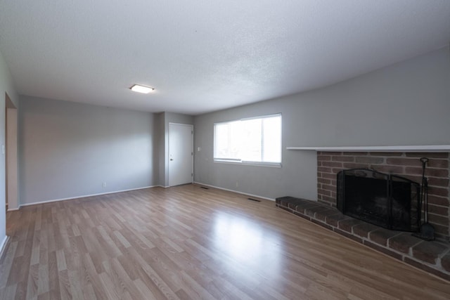 unfurnished living room featuring visible vents, baseboards, wood finished floors, a textured ceiling, and a brick fireplace