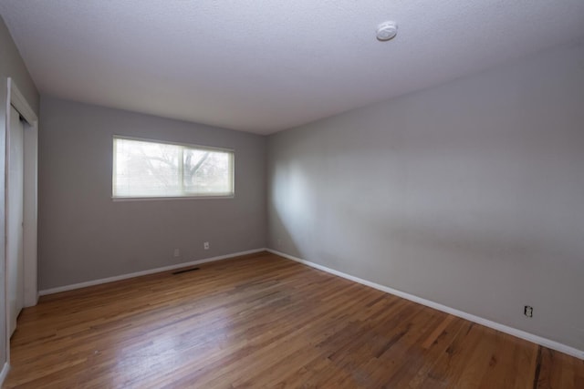 spare room with baseboards, visible vents, and wood finished floors