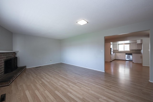 unfurnished living room with visible vents, a fireplace, light wood-style flooring, and baseboards