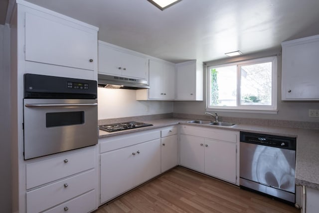 kitchen featuring light wood-style flooring, under cabinet range hood, stainless steel appliances, a sink, and light countertops