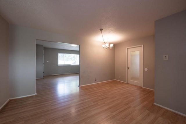 unfurnished room featuring light wood finished floors, baseboards, a chandelier, and a textured ceiling