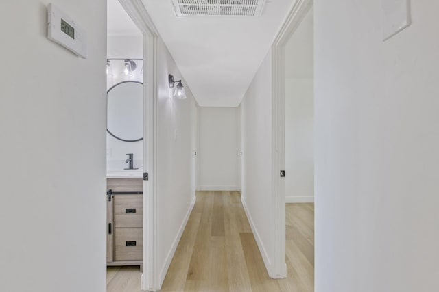 corridor with light wood-type flooring, baseboards, and visible vents