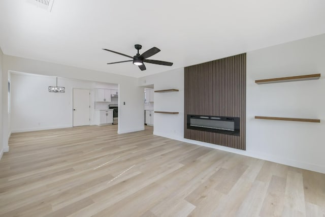 unfurnished living room featuring light wood finished floors, baseboards, a glass covered fireplace, and ceiling fan with notable chandelier