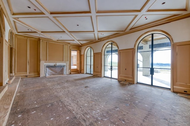 unfurnished living room with coffered ceiling, plenty of natural light, a decorative wall, and a fireplace