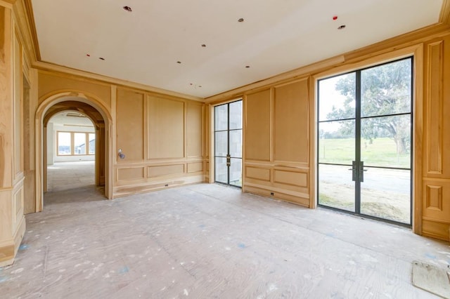 unfurnished room with arched walkways, a healthy amount of sunlight, crown molding, and a decorative wall