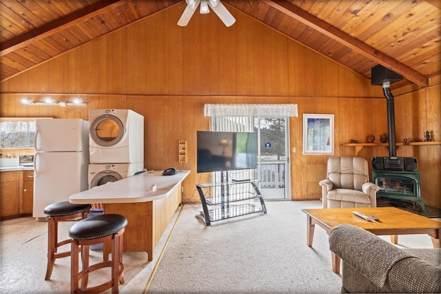 39118 Lake Dr, Bass Lake, CA 93604 - living area featuring stacked washing machine and dryer, a wood stove, wooden walls, a wooden ceiling with exposed beams, and high vaulted ceiling