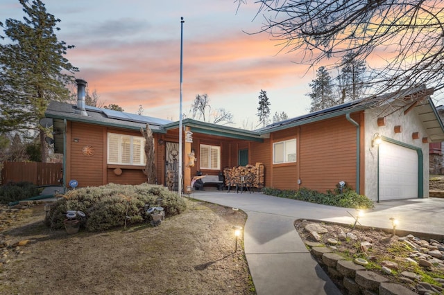 ranch-style house with roof mounted solar panels, fence, driveway, and an attached garage