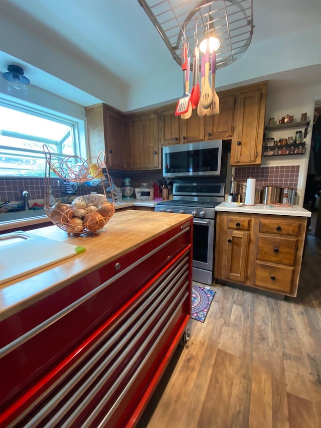 kitchen with light wood-style flooring, stainless steel appliances, butcher block counters, brown cabinets, and tasteful backsplash