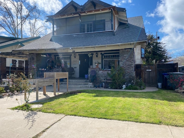 view of front facade featuring covered porch, a shingled roof, fence, and a front lawn