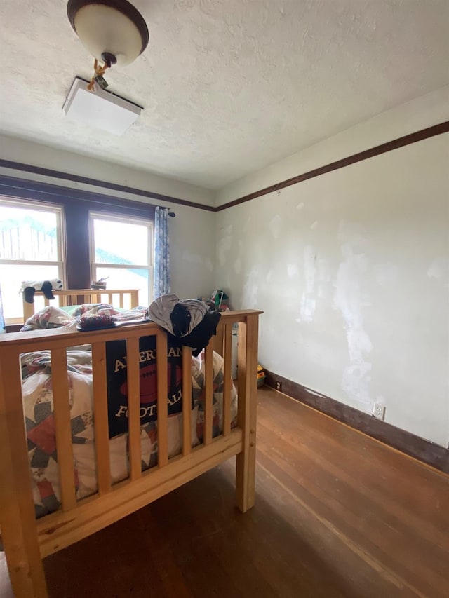 bedroom with a textured ceiling, wood finished floors, and baseboards