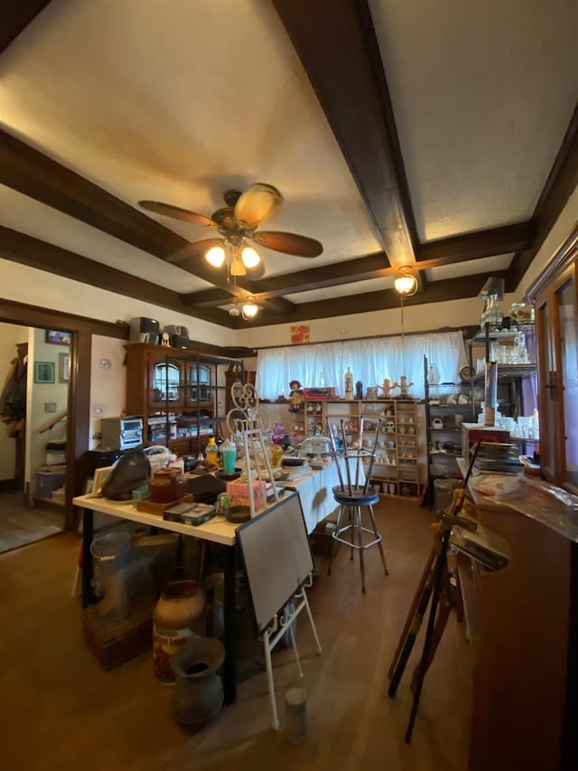 dining space with a ceiling fan, beamed ceiling, and wood finished floors