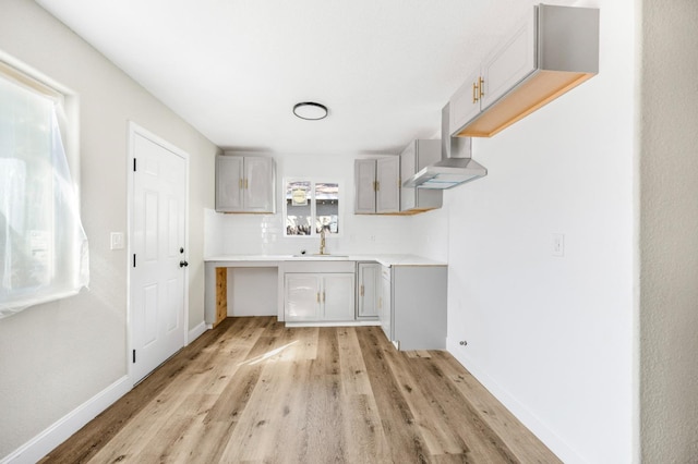 kitchen with gray cabinets, a sink, light wood-type flooring, baseboards, and exhaust hood