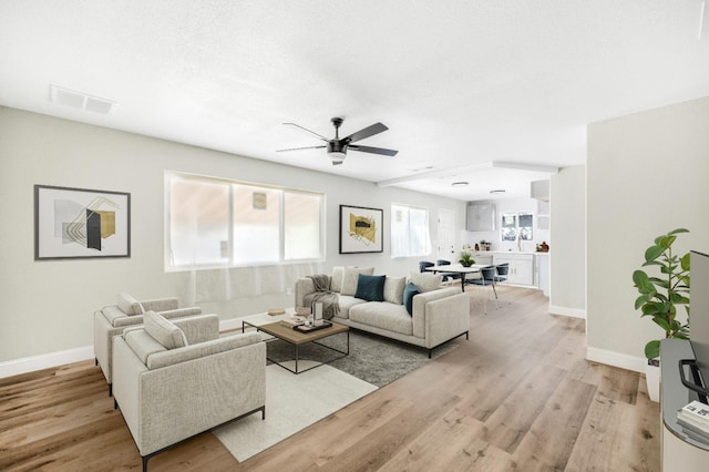 living room with light wood-type flooring, baseboards, visible vents, and a ceiling fan