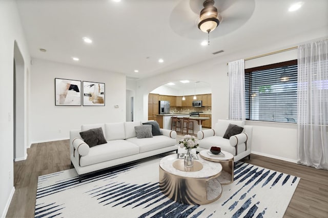 living area featuring baseboards, arched walkways, wood finished floors, and recessed lighting