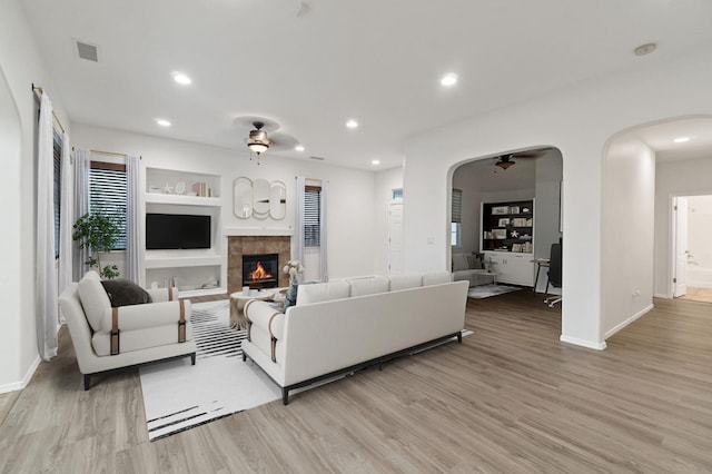 living area featuring arched walkways, built in features, ceiling fan, light wood-type flooring, and recessed lighting