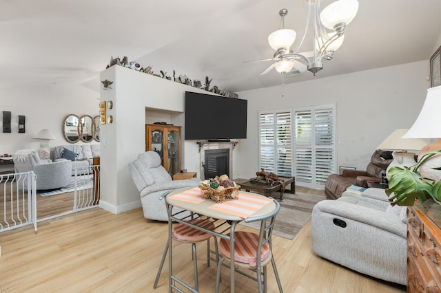 living area with a glass covered fireplace, light wood finished floors, and ceiling fan with notable chandelier