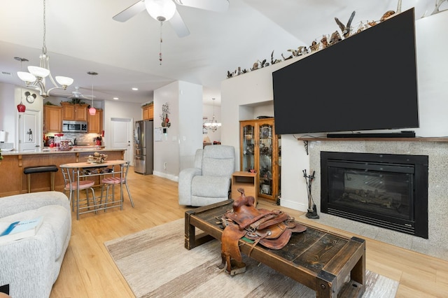 living room featuring recessed lighting, light wood-style floors, a glass covered fireplace, baseboards, and ceiling fan with notable chandelier